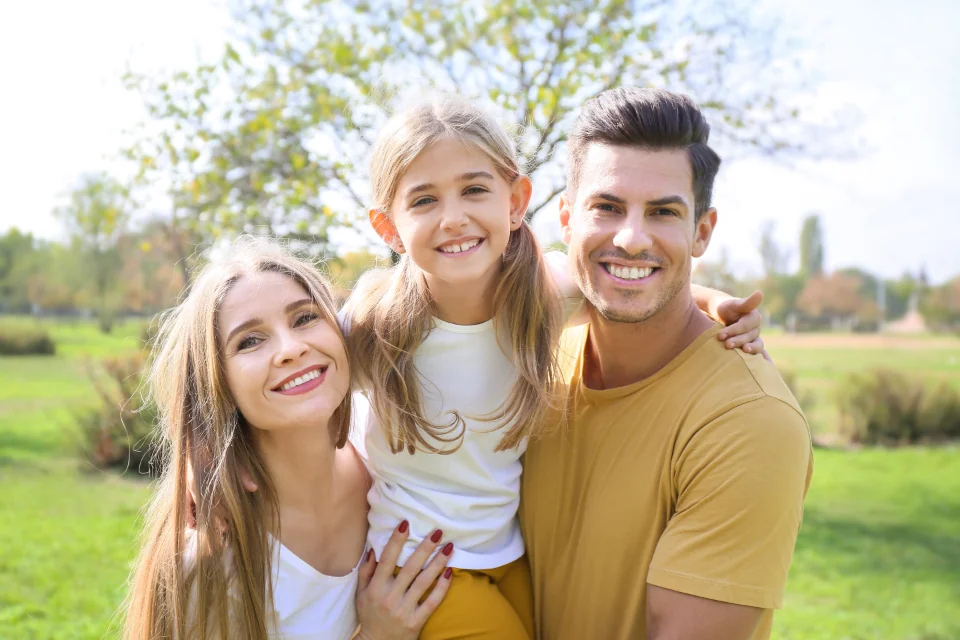 Three people posing together on a lawn with trees behind them