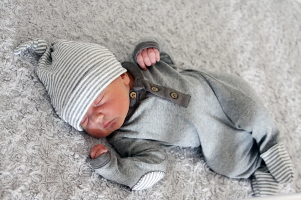 A clothed baby resting on a gray blanket