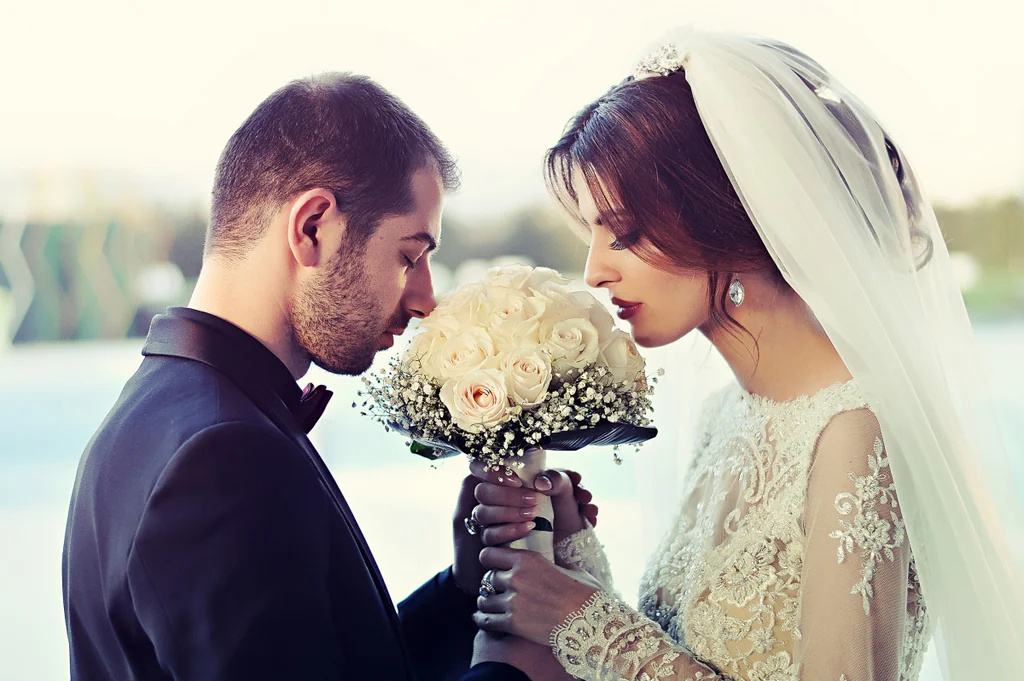 A wedding couple facing one another with a bouquet between them