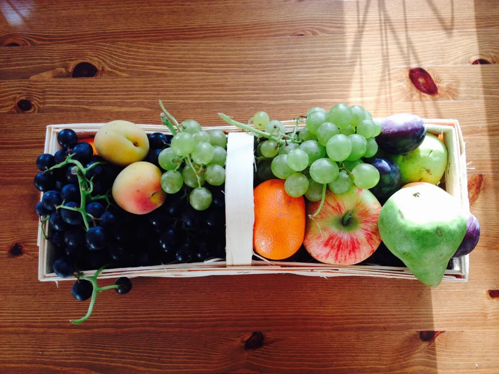 A wooden basket holding grapes, apples, pears, citrus and small round fruit