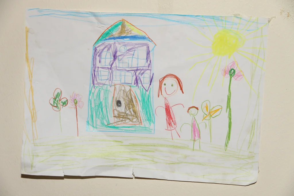 A colored pencil drawing on paper of a house, a sun, two people and flowers