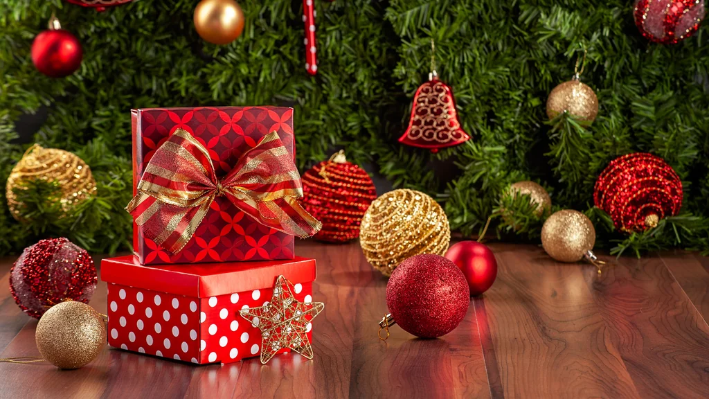 Two red gift boxes with a bow, red and gold baubles, a bell and a star in front of Christmas tree branches