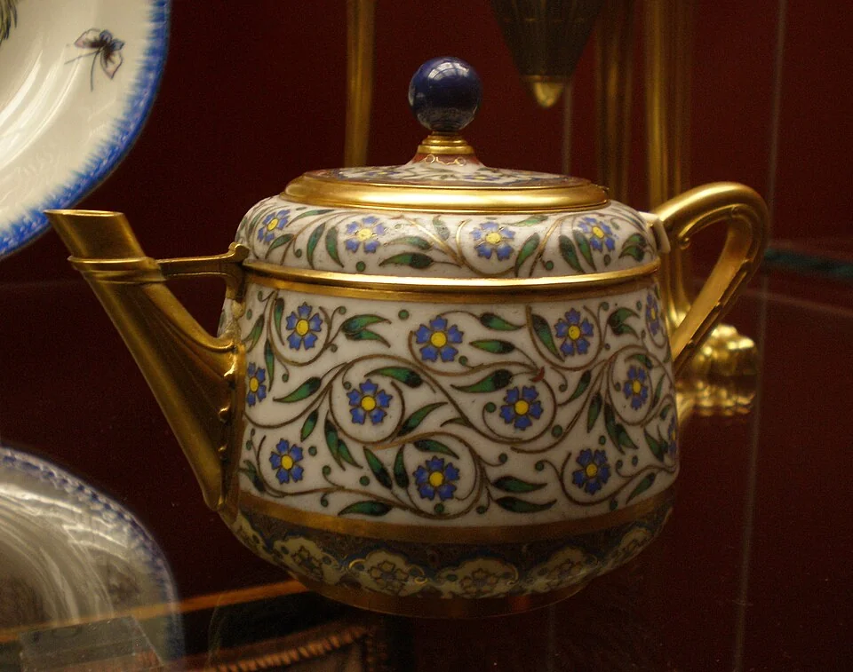 A floral enamel teapot with a lid, a left spout and a right handle